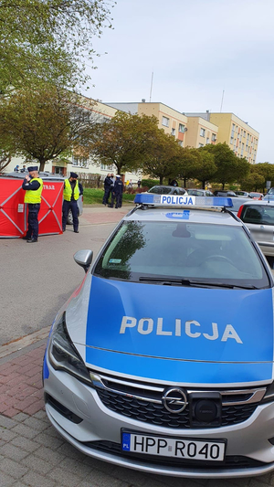 Radiowóz policyjny, a za nim policjanci i czerwony parawan.