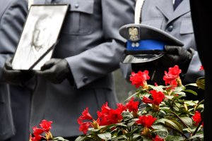 Zdjęcie pamiątkowe policjanta z kirem oraz czapka policyjna. Rzeczy trzymają w rękach policjanci z kompanii honorowej.