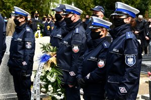 Policjanci na cmentarzu oczekują z wieńcem, by złożyć je na grobie.