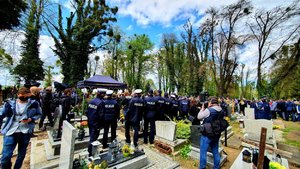 Na zdjęciu osoby uczestniczące w ceremonii pogrzebowej. Widoczni policjanci, dziennikarze i inne osoby, które przyszły pożegnać policjanta.