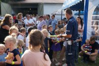 Policjant z drogówki rozdaje elementy odblaskowe na festynie rodzinnym