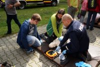 Policjant omawia zgromadzonym dzieciom zasady udzielania pierwszej pomocy przedmedycznej