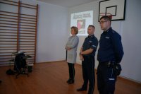 Policjanci stoją wspólnie z dyrektor szkoły w Budziskach witają zgromadzone dzieci na spotkaniu