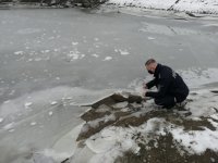 Policjant kuca nad zamarznietymzbiornikiem wodnym pokazując grubość lodu