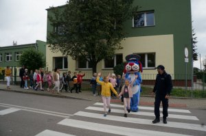 Raciborski policjant wspólnie z dziećmi i policyjną maskotką przechodzą przez przejście dla pieszych