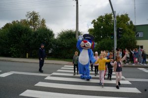 Raciborski policjant wspólnie z dziećmi i policyjną maskotką przechodzą przez przejście dla pieszych