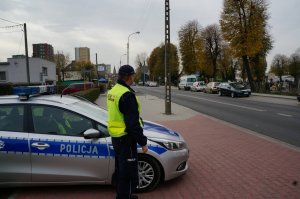 Policjant na tle radiowozu przy cmentarzu