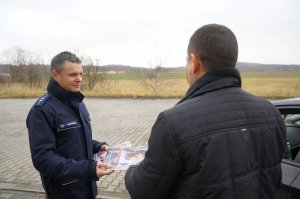 Policjant z raciborskiej drogówki wręcza kierowcy odblaski i ulotkę