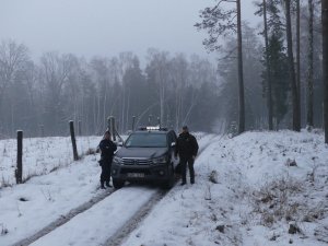 Policjantka wspólnie ze strażnikiem leśnym na tle lasu i samochodu słuzbowego