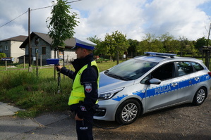 Policjant z drogówki na tle radiowozu mierzy prędkość urządzeniem