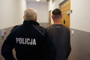 Policjant stoi obok zatrzymanego związanego z pobiciem