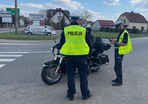 Policjanci z drogówki stoja przy zatrzymanym do kontroli drogowej motocykliście