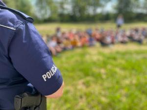 Dzieci siedzą na trawie i słuchają porad policjanta