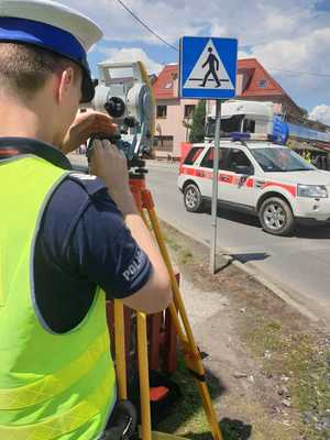 Policjant z tachimetrem oraz w tle widoczny radiowóz straży pożarnej