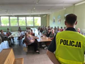 Widok sali z seniorami i policjanta prowadzącego pogadankę o bezpieczeństwie