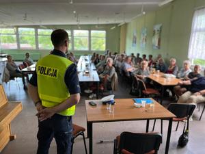 Widok sali z seniorami i policjanta prowadzącego pogadankę o bezpieczeństwie