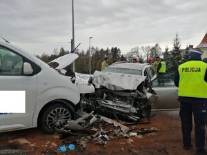 Widok dwóch pojazdów, które się zderzyły, rozbite samochody na środku drogi oraz policjant z drogówki w czasie czynności