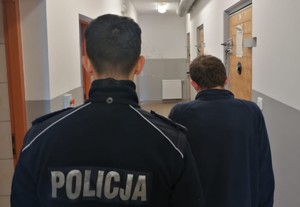 Policjant stoi obok zatrzymanego mężczyzny związanego z posiadaniem narkotyków