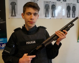 Uczeń ubrany w policyjną kamizelkę kuloodporną w ręku ze strzelbą