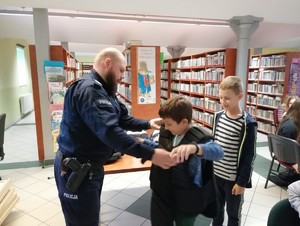 na zdjęciu policjant pomagający ubrać kamizelką dziecku
