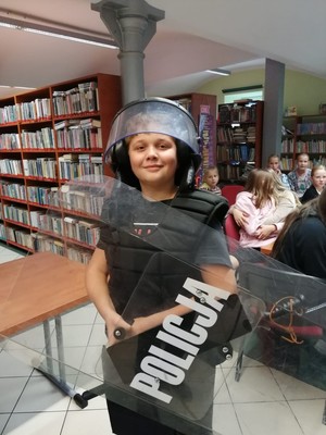 na zdjęciu chłopiec ubrany  w policyjny kask, kamizelkę, trzymający tarczę
