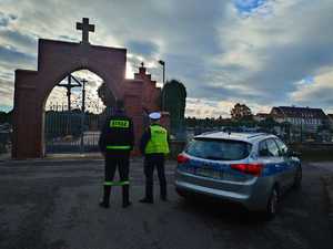 na zdjęciu policjant i strażak przy cmentarzu