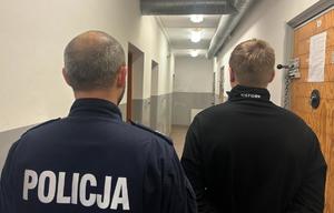 na zdjęciu zatrzymany mężczyzna z policjantem stoją tyłem