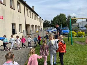 na zdjęciu dzieci trzymają policjanta za rękę i tańczą w kółeczku do piosenki