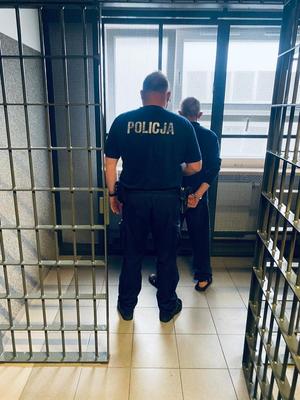 na zdjęciu policjant i zatrzymany mężczyzna stoją tyłem