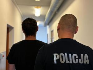 na zdjęciu zatrzymany mężczyzna i policjant stoją tyłem