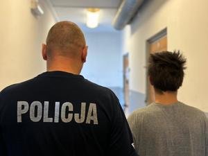 na zdjęciu zatrzymany mężczyzna z policjantem stoją tyłem