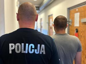 na zdjęciu zatrzymany mężczyzna stoi z policjantem tyłem