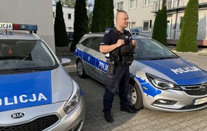 na zdjęciu policjant na tle radiowozów