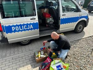 na zdjęciu policjant w ubraniu cywilnym pakuje dary do auta