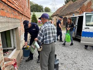 na zdjęciu policjanci rozdają potrzebne rzeczy powodzianom