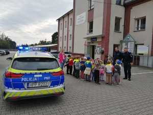 na zdjęciu przedszkolaki przed posterunkiem policji w tle radiowóz i policjanci