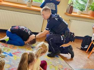 na zdjęciu policjant ćwiczy z dziećmi jak bezpiecznie uchronić się przed atakiem psa