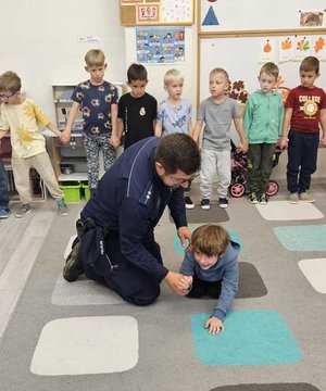 na zdjęciu policjant ćwiczy z dziećmi pozycję bezpieczna przed ugryzienie przez psa