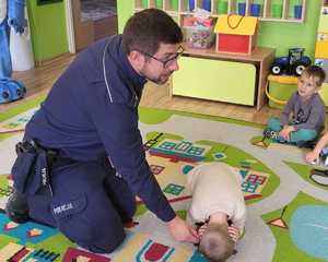 na zdjęciu policjant pokazuje jak uchronić się gdy zaatakuje nas groźny pies dzieci ćwiczą pozycje