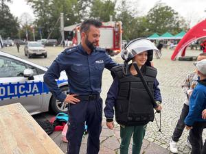 na zdjęciu policjant i chłopczyk przymierza sprzęt policyjny