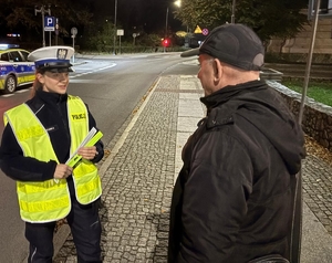 na zdjęciu policjantka rozdaje panu odblask