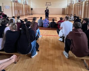 na zdjęciu policjant prowadzi pogankę uczniowie na krzesełkach