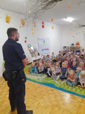 na zdjęciu policjant i przedszkolaki na dywanie słuchają pogadanki