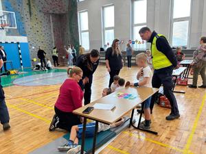 na zdjęciu policjantka i policjant pomagają przedszkolakom ułożyć pozycje bezpieczna