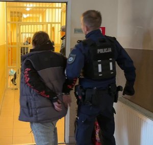 na zdjęciu policjant z zatrzymana kobieta stoją tyłem