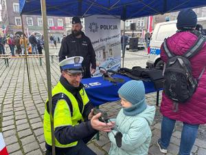 na zdjęciu policjant ruchu drogowego pokazuje dziecku broń i rozmawia z uczestnikami pikniku