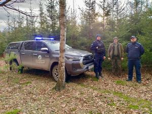 na zdjęciu policjant strażnik leśny i radiowóz ze straży leśnej przy choinkach