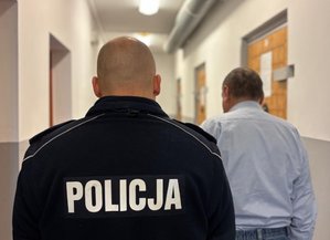 na zdjęciu zatrzymany mężczyzna stoi tyłem a policjant obok