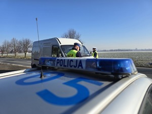 na zdjęciu policjant ruchu drogowego kontroluje białego busa