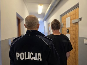 na zdjeciu zatrzymany z policjantem stoja tyłem